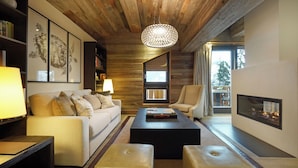 A modern living room with a wooden ceiling, a round chandelier, a sofa, a coffee table, and a fireplace. - The Lodge Verbier (Bagnes)