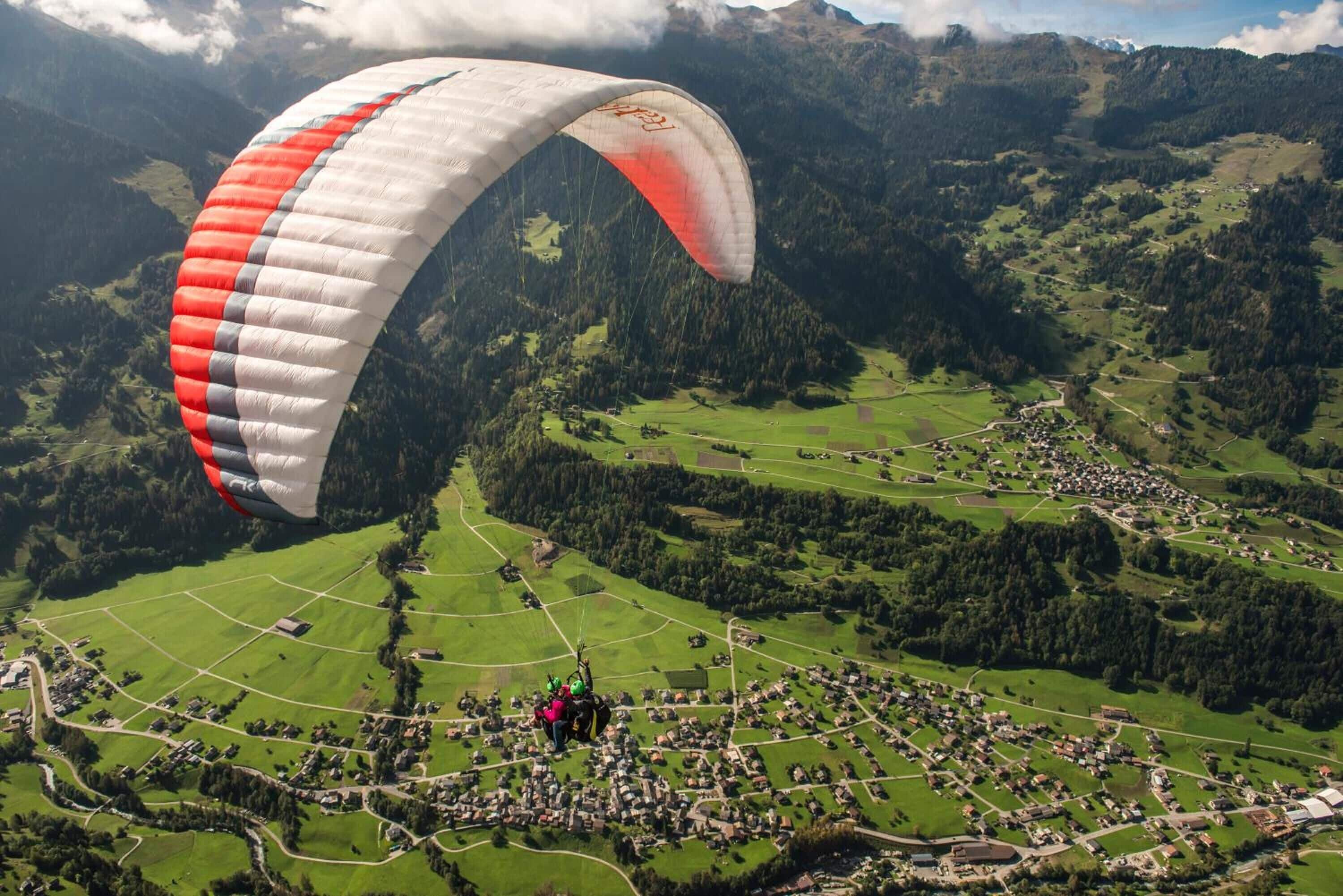 A person paragliding over a rural landscape with fields and a small village below.