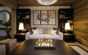 A cozy living room with a sofa, a coffee table with a board game, and two side tables with lamps. - The Lodge Verbier (Bagnes)
