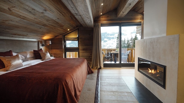 A bedroom with a large bed, a fireplace, and a view of mountains through a sliding glass door. - The Lodge Verbier (Bagnes)