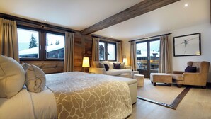 A spacious bedroom with a large bed, a sofa, a chair, and a view of a snowy landscape through the windows. - The Lodge Verbier (Bagnes)