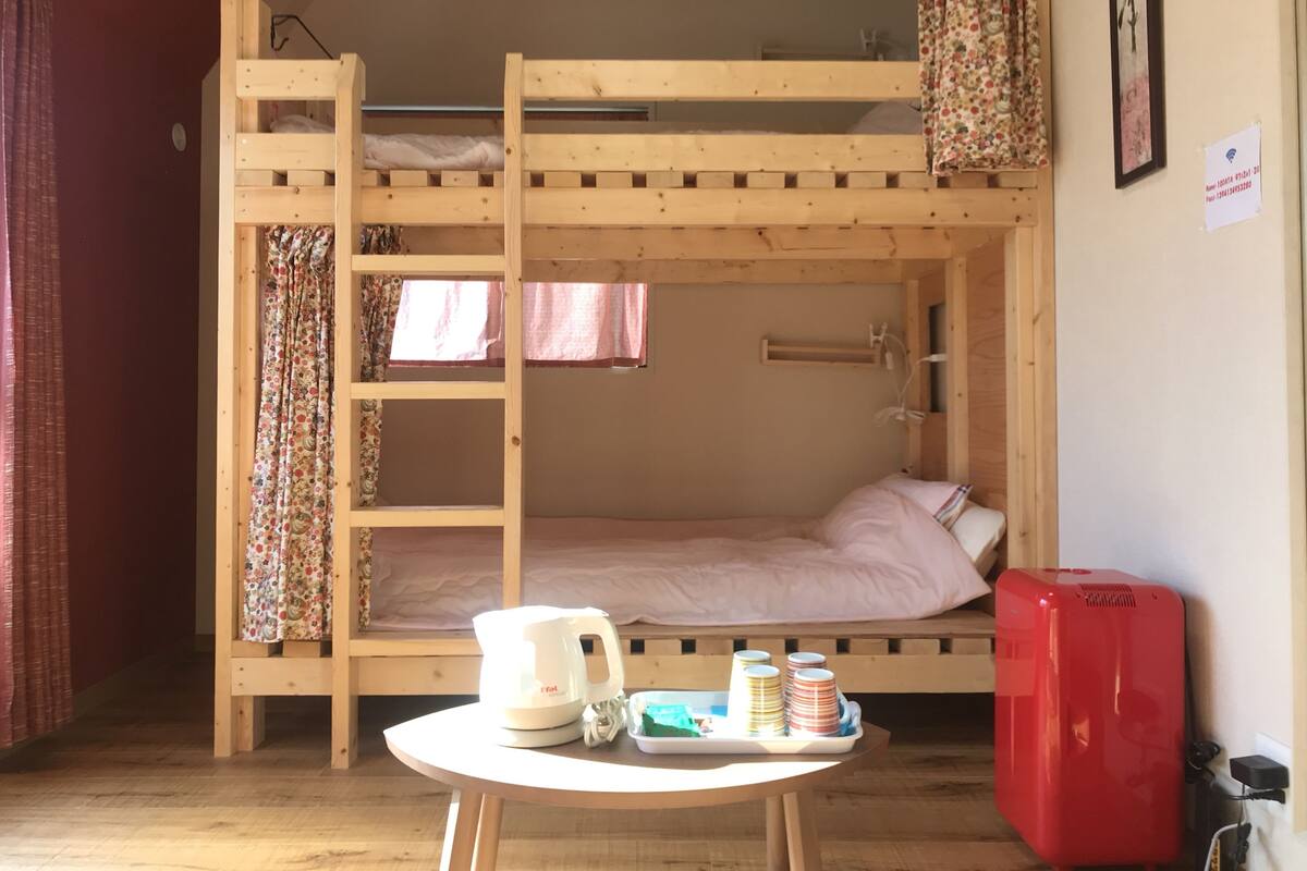 Habitación con literas, una mesa en el centro, una tetera y una maleta roja.