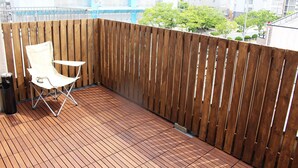 A balcony with a wooden fence, a white folding chair, and a tiled floor.
