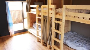 A room with two bunk beds, a window with curtains, and a wooden floor.