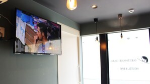 A hotel room with a television mounted on the wall, a door with a sign, and pendant lights.