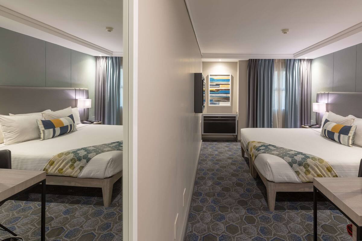A hotel room with two beds, a TV, a painting, and a patterned carpet.