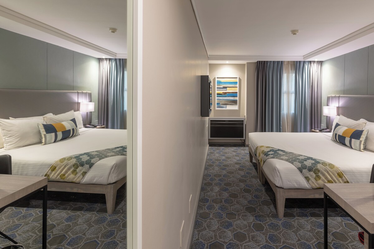 A hotel room with two beds, a flat-screen TV mounted on the wall, and a patterned floor.