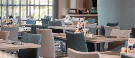A modern restaurant with multiple tables and chairs, large windows, and a clean, minimalist interior design.