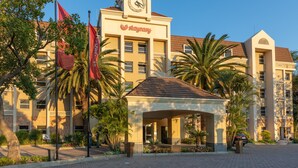 Un hotel con torre del reloj, palmeras y entrada cubierta.