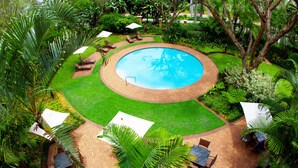 A circular pool surrounded by a brick patio with lounge chairs and umbrellas. - StayEasy Mbombela (Mbombela)