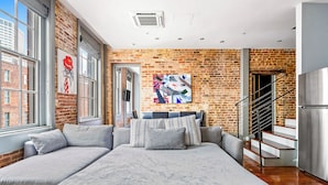 A modern living room with a large sectional sofa, a brick wall, and a staircase. - Heated Pool, Hot Tubs, & Style Near French Qtr – Great for Families & Groups (New Orleans)