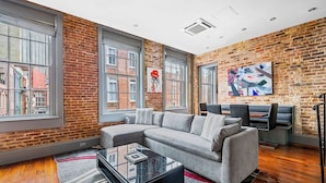 A modern living room with a grey sectional sofa, a glass coffee table, and a brick wall. - Heated Pool, Hot Tubs, & Style Near French Qtr – Great for Families & Groups (New Orleans)