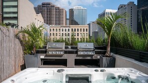 A rooftop patio with two gas grills, a hot tub, and a city skyline in the background. - Heated Pool, Hot Tubs, & Style Near French Qtr – Great for Families & Groups (New Orleans)