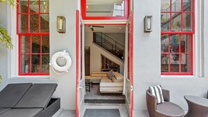 A modern hotel entrance with a red-framed door, a visible staircase leading to an upper level, a lounge area with a sofa and chairs, and a lifebuoy on the wall. - Poolside 3BR w Hot Tubs, Grill Near French Qtr, Great for Families & Groups (New Orleans)