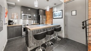 A modern kitchen with grey cabinets, stainless steel appliances, a central island with bar stools, and pendant lighting. - Poolside 3BR w Hot Tubs, Grill Near French Qtr, Great for Families & Groups (New Orleans)