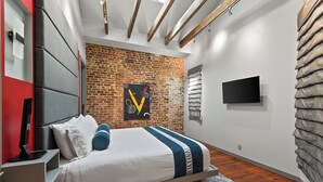 Une chambre moderne avec un mur en briques, un grand lit recouvert d’une couverture à rayures, un téléviseur fixé au mur et un mur d’accent de couleur rouge.