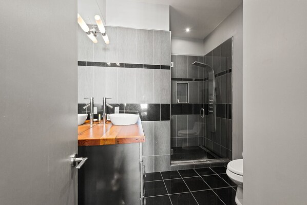 Un baño moderno con un tocador de madera, un lavamanos blanco y un box de ducha de vidrio.