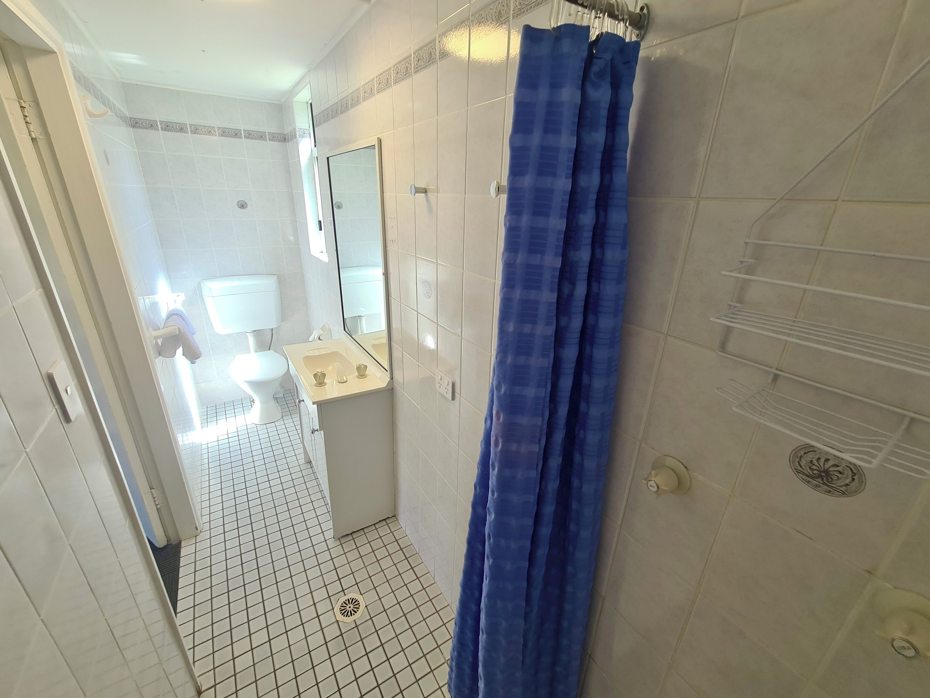 A bathroom with a white toilet, a sink, and a mirror. There is a blue shower curtain and a white towel rack.
