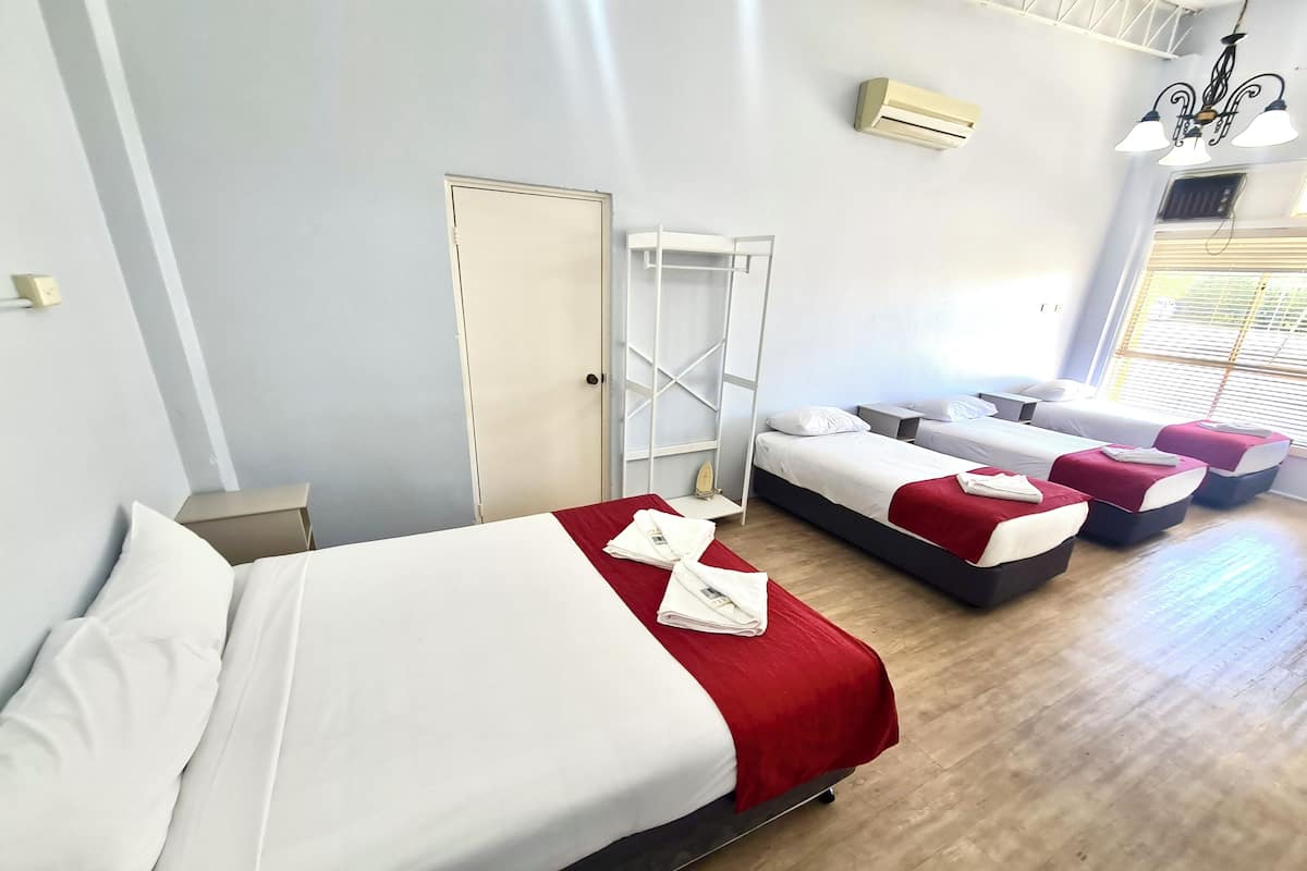 A hotel room with a large bed, two smaller beds, a wardrobe, and a window with blinds.