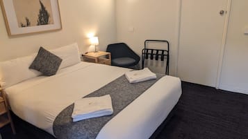 A hotel room with a bed, a nightstand, a chair, a wall-mounted towel rack, and a framed picture on the wall.