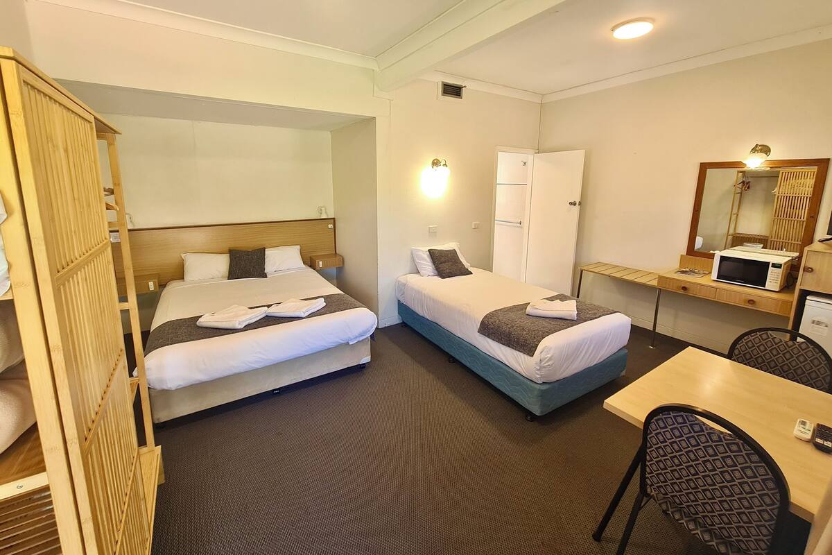 A hotel room with two beds, a desk, a microwave, and a mirror.