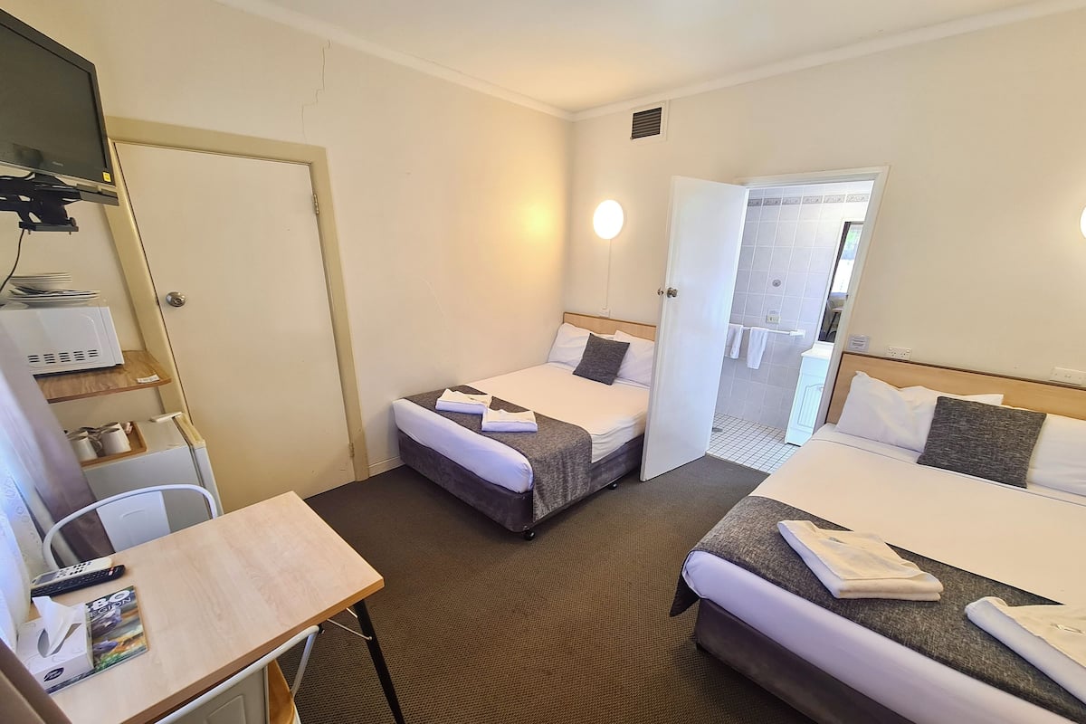 A hotel room with two beds, a desk, a chair, a microwave, and a bathroom visible through an open door.