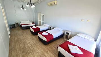 A hotel room with three beds, each with white and red bedding, a wooden floor, and a ceiling fan.