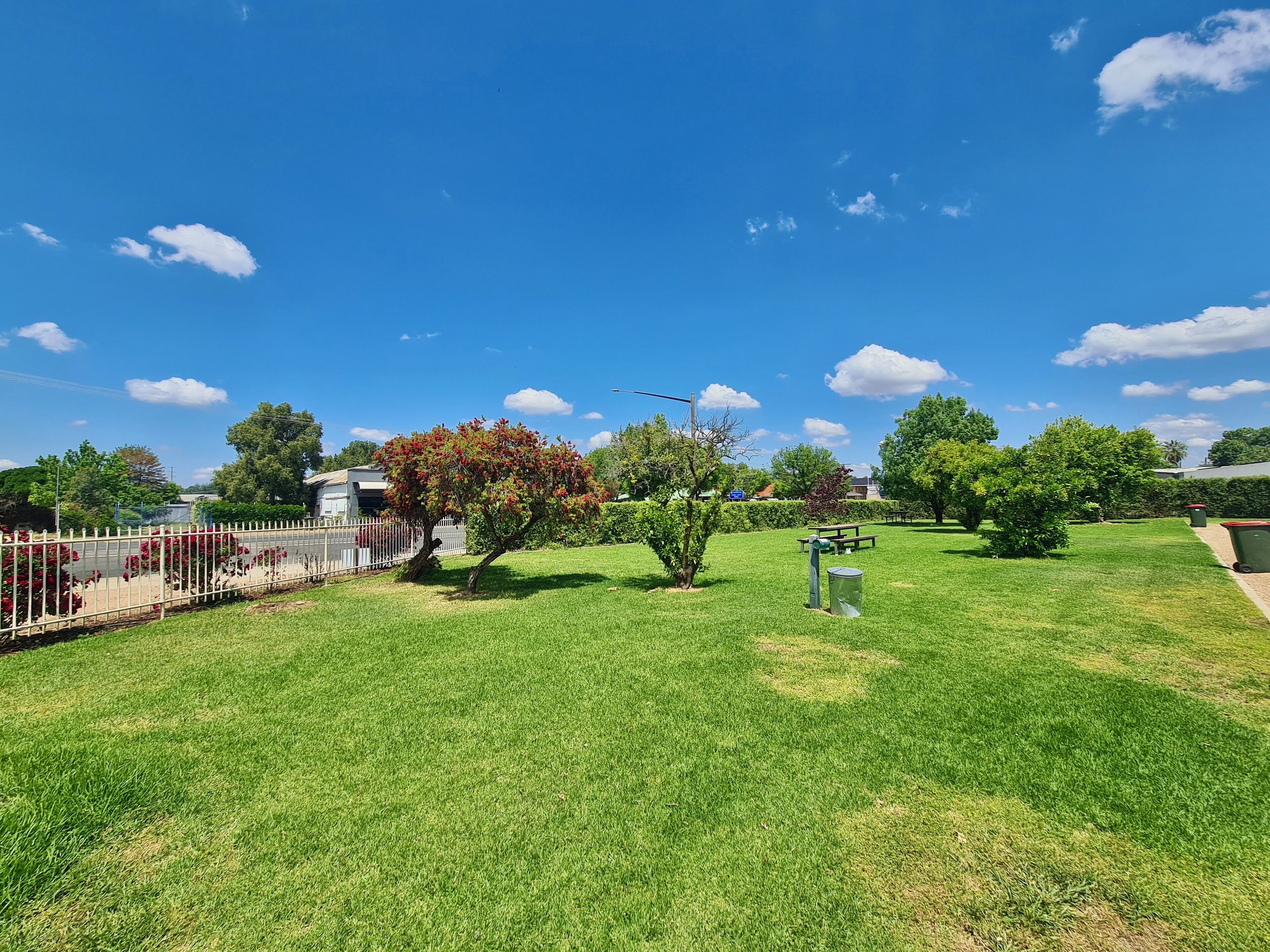 A well-maintained grassy area with a fenced section, trees, and a bench.