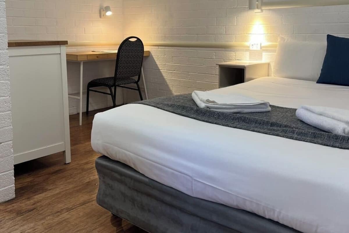 A hotel room with a bed, a desk, a chair, and a ceiling fan.