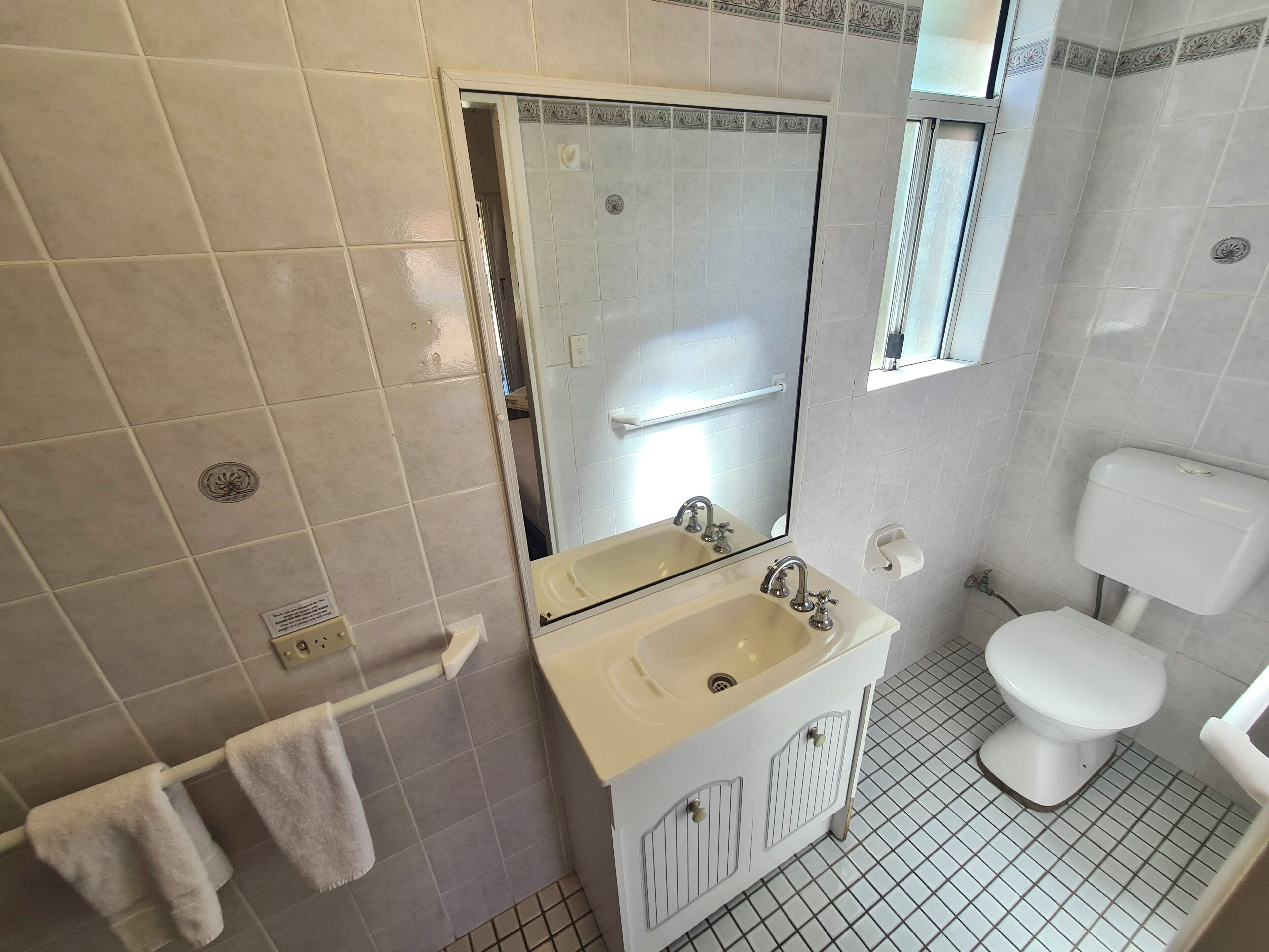 A bathroom with a white sink, mirror, and toilet. There is a towel rack with two towels.