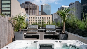 A rooftop patio with two gas grills, a hot tub, and a city skyline in the background.