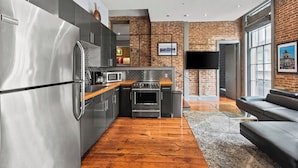 A modern kitchen with stainless steel appliances, a brick wall, and a wooden floor.