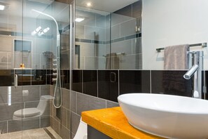 A modern bathroom with a glass-enclosed shower, a white sink, and a wooden countertop. - Private Hot Tub, Patio, & Grill! Heated Pool in Courtyard, Family Friendly (New Orleans)