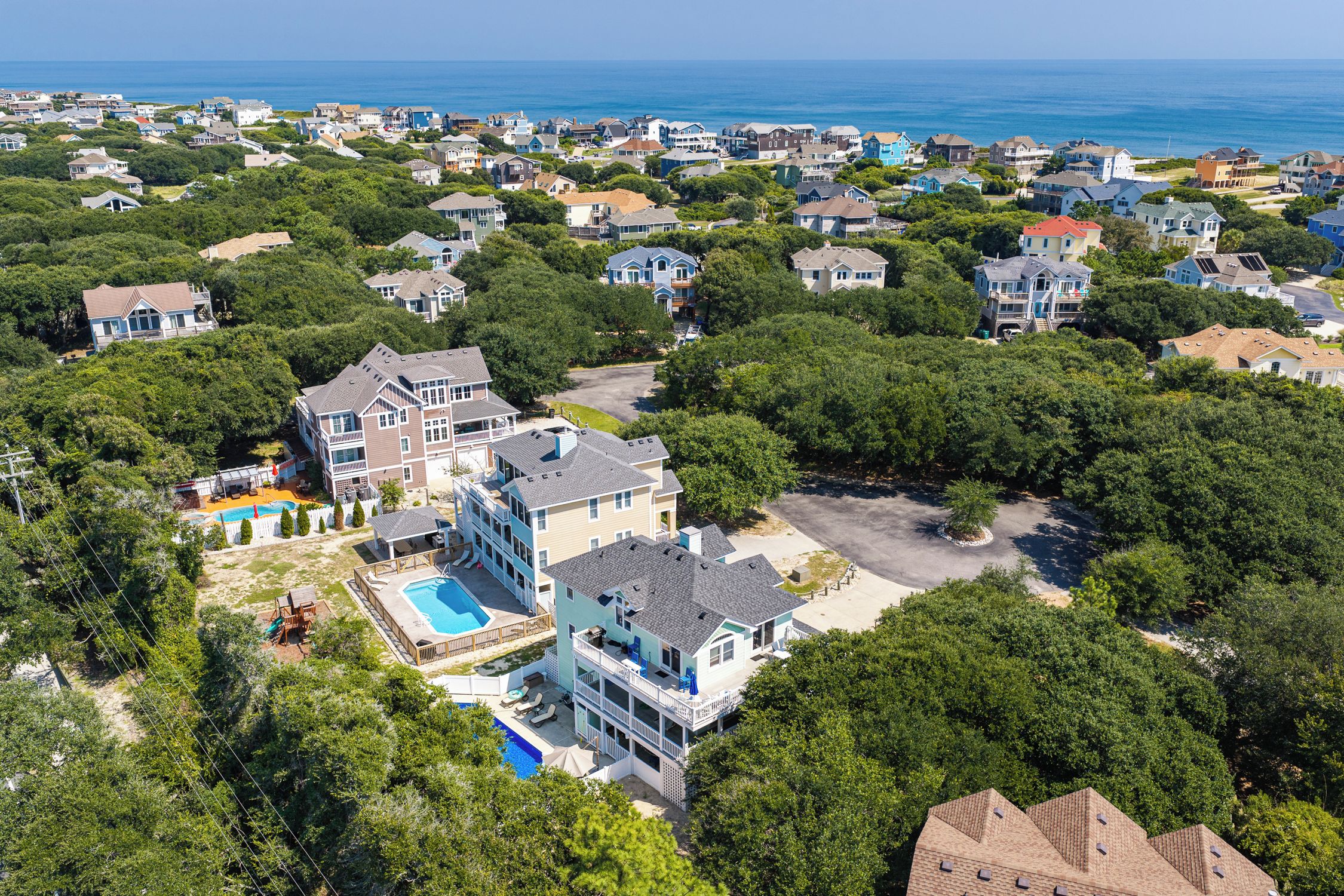 A residential area with multiple houses, a swimming pool, and a view of the ocean.
