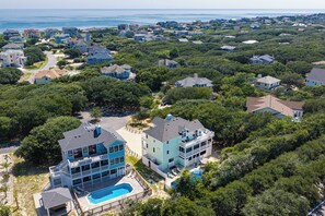 A residential area with houses surrounded by greenery, a clear sky, and a view of the sea.