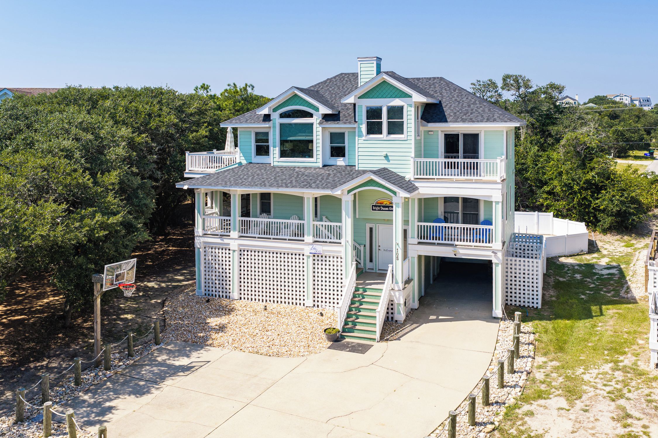 A two-story house with a balcony, a front porch, and a driveway leading to a gated entrance.