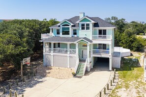 A two-story house with a balcony, a front porch, and a driveway leading to a gated entrance.