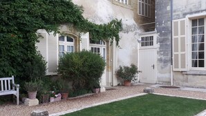 A building with white shutters, a small garden with potted plants, and a grassy lawn.