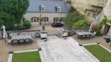 Un patio con mobiliario exterior, un coche estacionado frente a un edificio de fachada de piedra y techo inclinado.