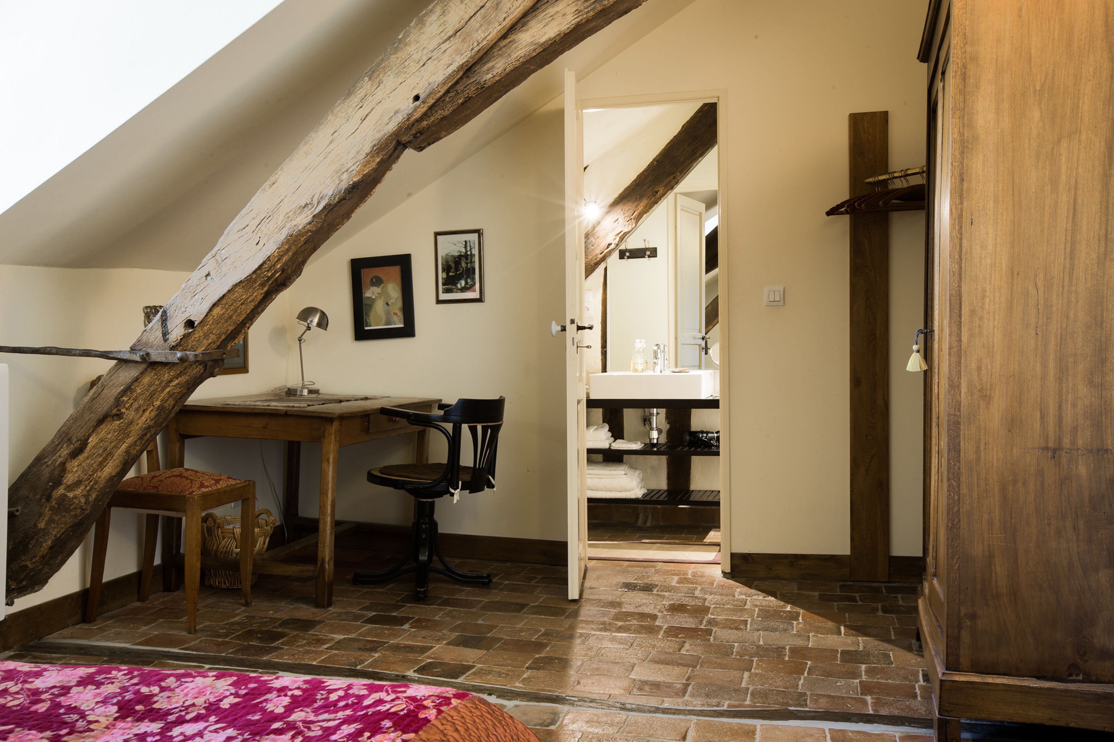 Un dormitorio estilo loft con vigas de madera a la vista, un escritorio, una silla y una cama con una manta rosa.