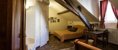 A bedroom with a sloped ceiling, a bed, a desk, and a chair.