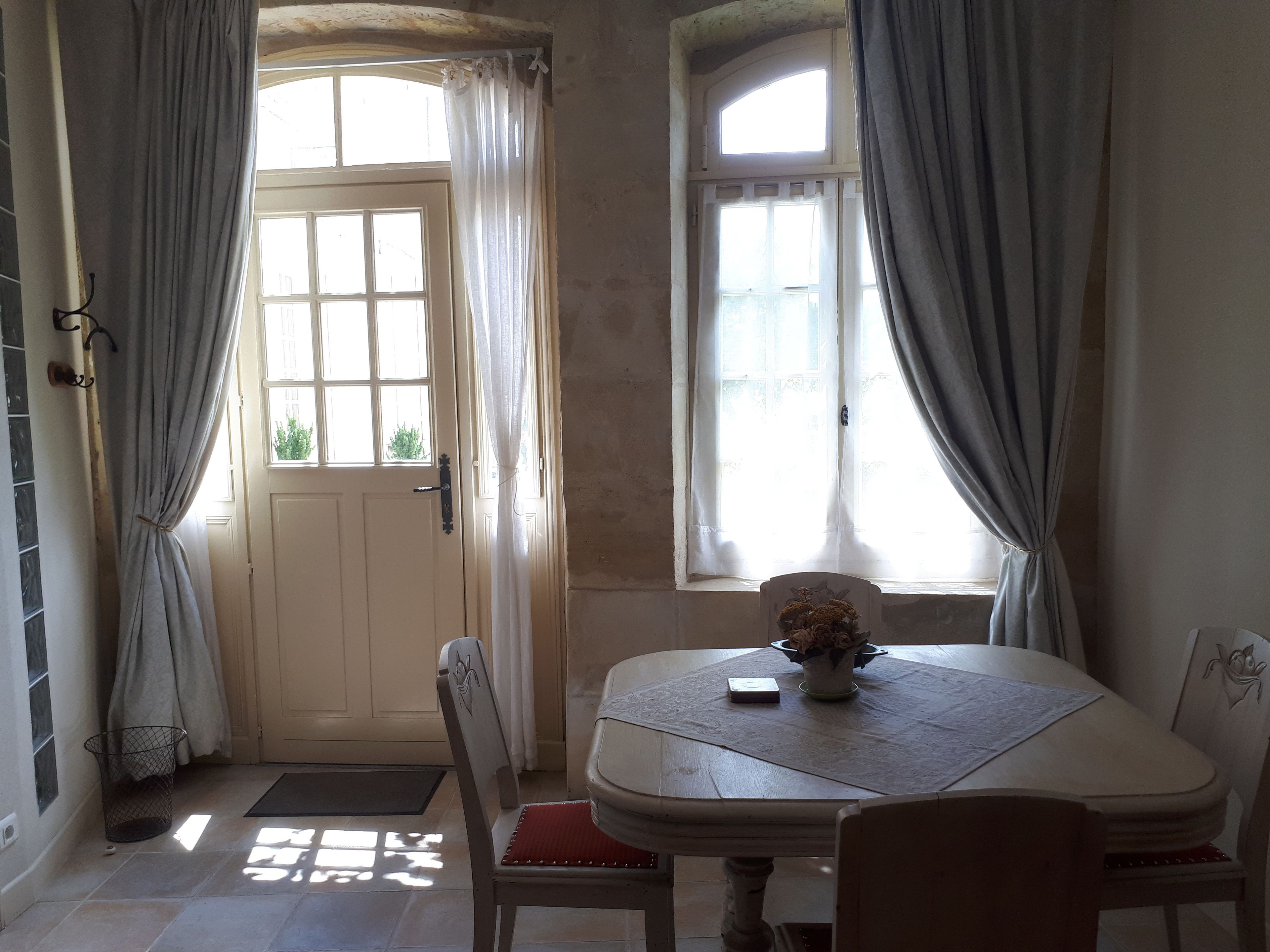 Un comedor con una mesa, sillas, un florero con flores y una ventana con cortinas.