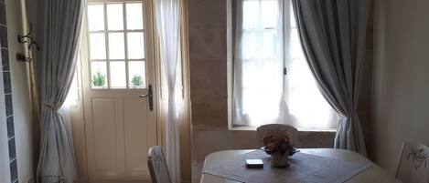 Un comedor con una mesa, sillas, un florero con flores y una ventana con cortinas.