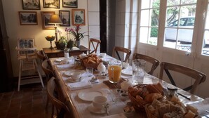 A dining table set for breakfast with bread, juice, and tea, surrounded by chairs and a high chair.