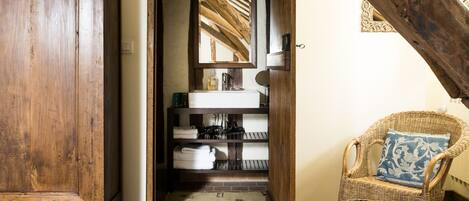 A rustic bathroom with a wooden door, a white sink, a mirror, and a wicker chair with a cushion.