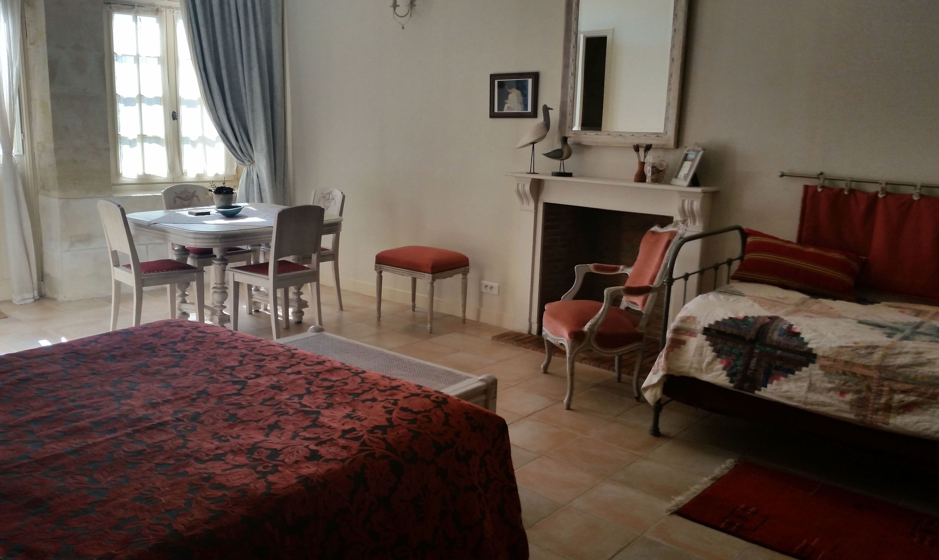 A bedroom with a bed, a desk with chairs, a fireplace, and a window with curtains.