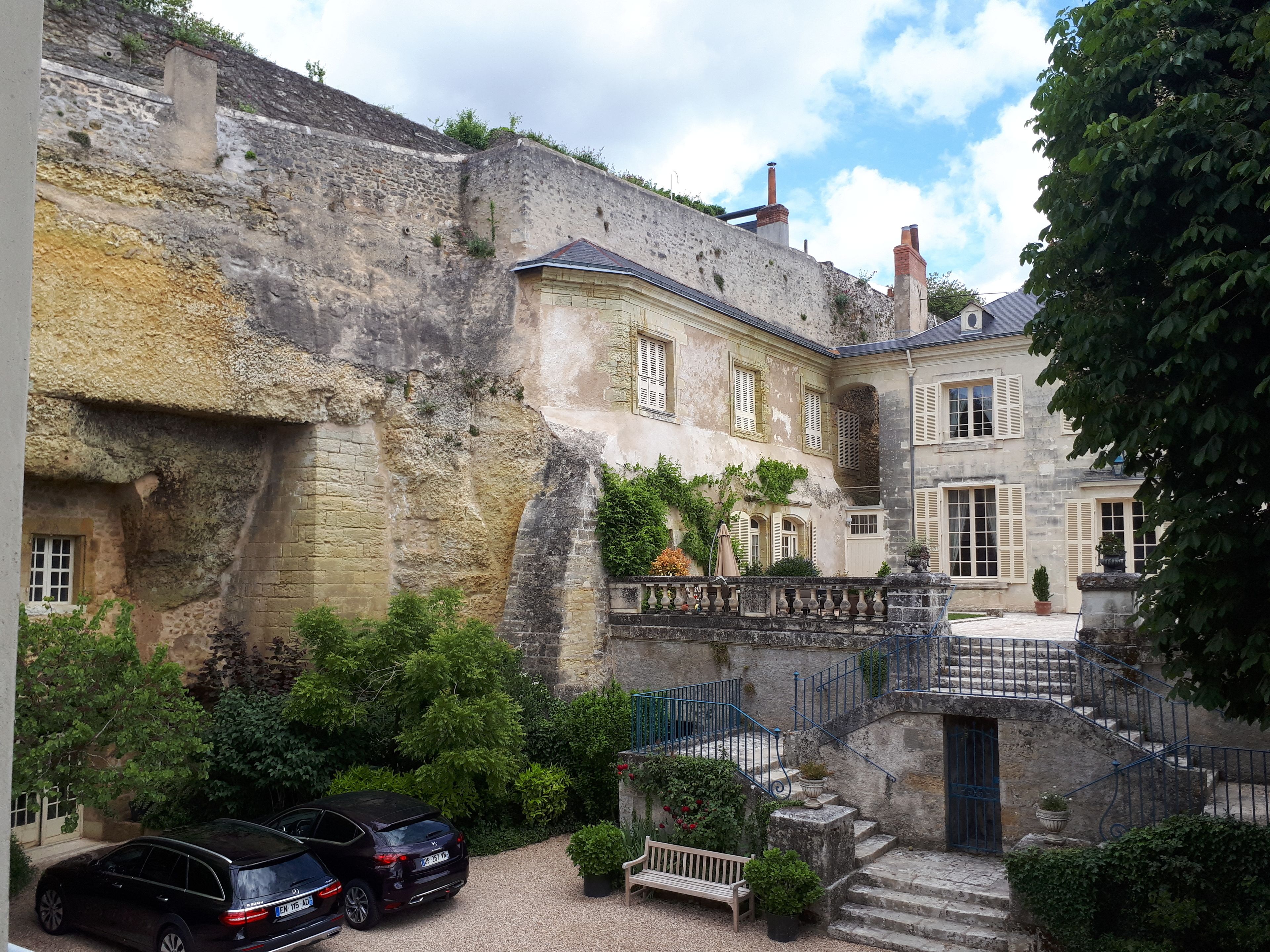 A courtyard with a stone wall, a staircase, and a building with multiple windows.