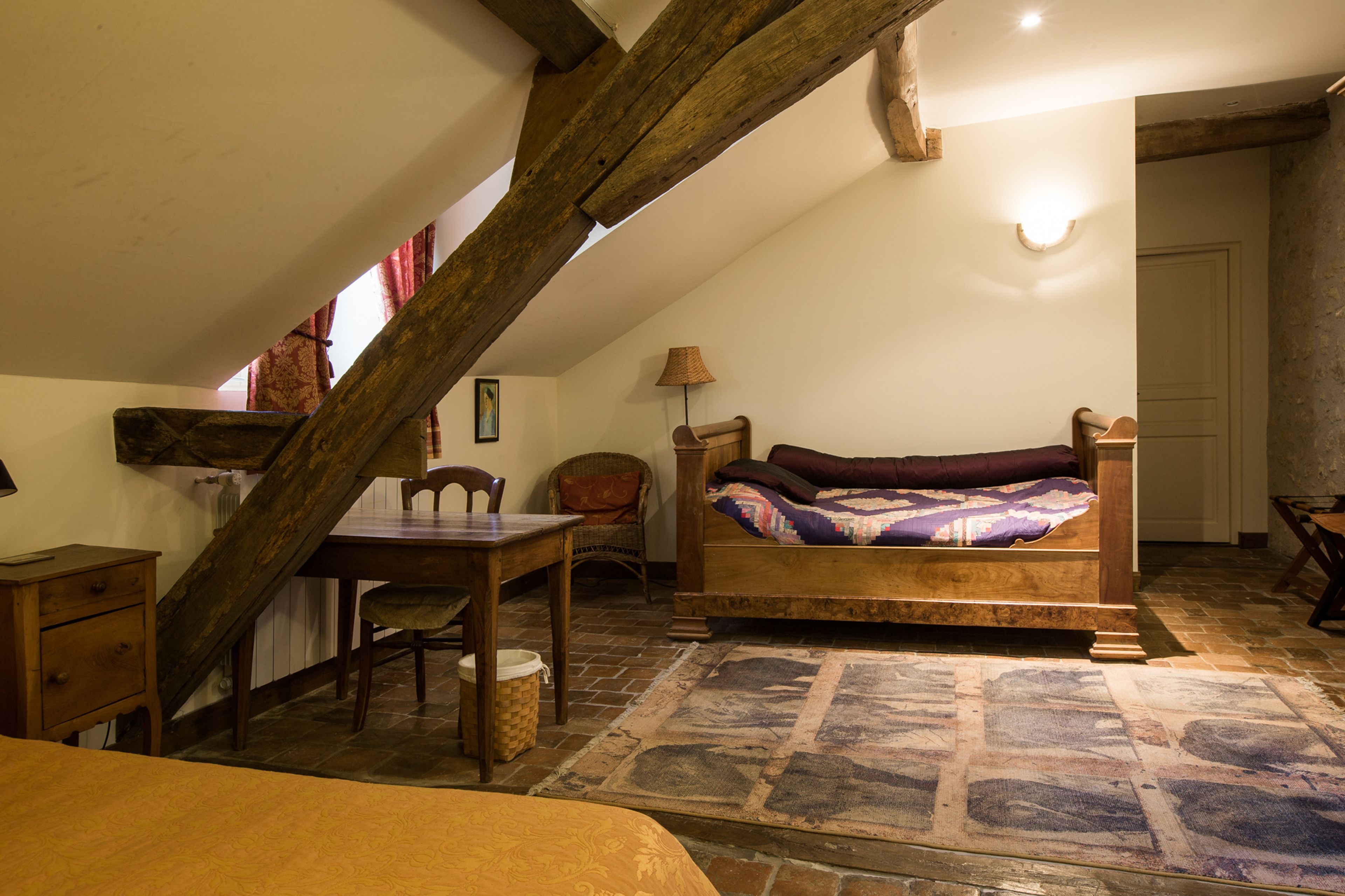 A cozy attic bedroom with a wooden bed, a small table, and a chair.