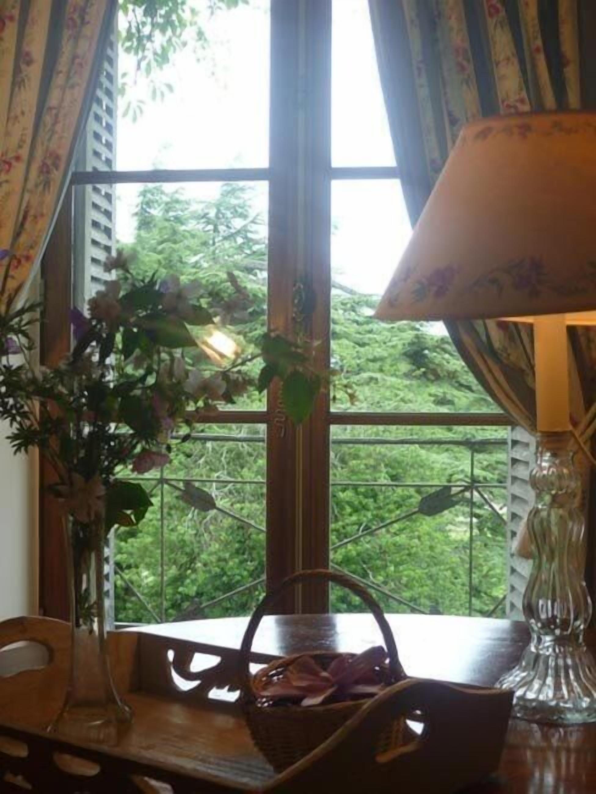 Una stanza con un'ampia finestra, un tavolo di legno, un cesto di vimini e una lampada.