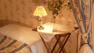 A bedroom with a bed, a bedside table with a lamp, a vase with flowers, and floral curtains.